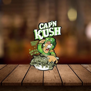 Può includere: Una ciotola di cereali verdi con la scritta "CAP'N KUSH" in verde e bianco. I cereali sono in una ciotola bianca. La scatola dei cereali presenta un personaggio dei cartoni animati in uniforme verde che saluta. È visibile anche la scritta "SWEETENED CANNABIS CEREAL".