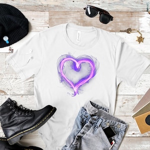 May include: White t-shirt with a purple heart design. The heart has a glowing, smoky effect. The image also shows blue jeans, black boots, and sunglasses. The shirt is made of a soft material.