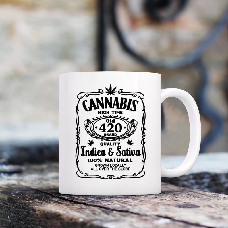 K&ouml;nnte beinhalten: Wei&szlig;e Keramik-Tasse mit schwarzem Grafikdesign. Das Design zeigt das Wort "CANNABIS", die W&ouml;rter "HIGH TIME", "Old 420 Brand", "Indica & Sativa" und "100% NATURAL". Die Tasse hat einen gebogenen Henkel.