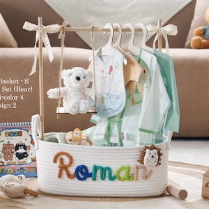 Puede incluir: Una cesta blanca de cuerda con el nombre "Roman" en letras coloridas. La cesta contiene ropa de bebé, un oso de peluche en un columpio y un calendario. El texto "White Basket - S Premium Set (Bear) Muliti-color 4 Design 2" es visible.