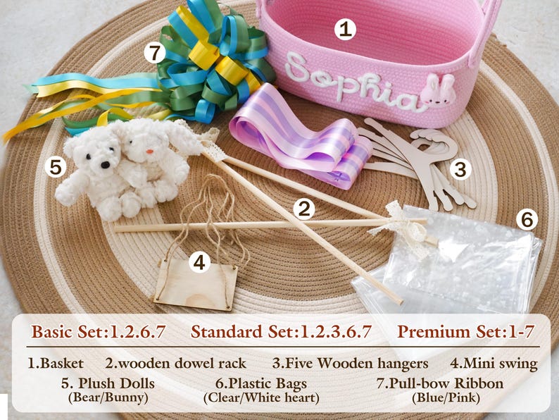 May include: A pink woven basket with the name "Sophia" in white script, surrounded by various craft supplies. Includes wooden dowel rods, hangers, plush dolls, a mini swing, plastic bags, and blue and pink pull-bow ribbon.