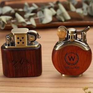 May include: Two vintage-style lighters with wooden bodies and brass accents. One is rectangular with "JACKSON" engraved, the other is round with "WILLIAM" and a "W" initial. Both have intricate metal mechanisms.