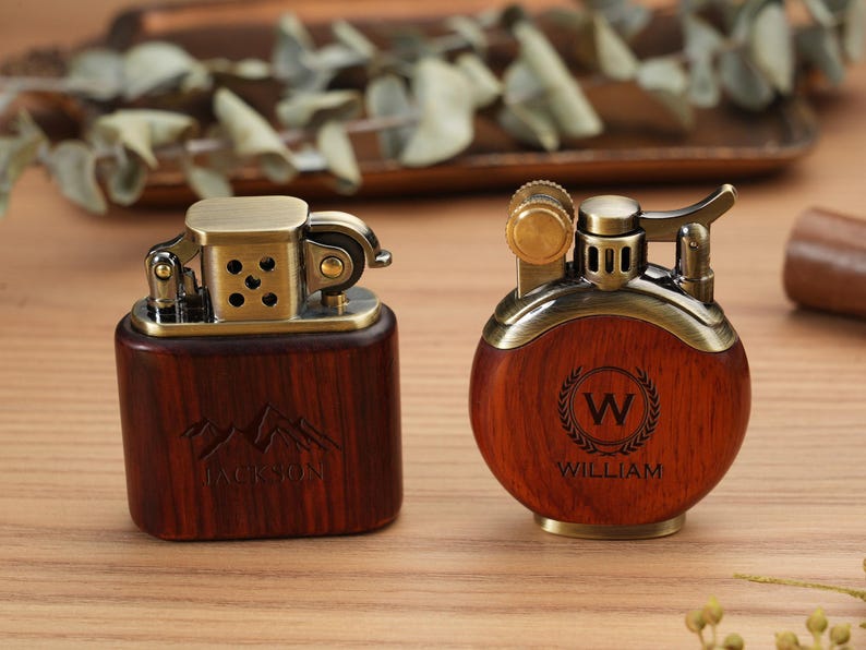 May include: Two vintage-style lighters with wooden bodies and brass accents. One is rectangular with "JACKSON" engraved, the other is round with "WILLIAM" and a "W" initial. Both have intricate metal mechanisms.