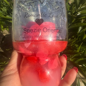 以下が含まれることがあります： 赤いキャンドルが入った透明なガラスのキャンドルホルダー。「Romantic Love」と「Spezie Orientali」のラベルが付いています。キャンドルはピンクと赤色の液体で満たされています。