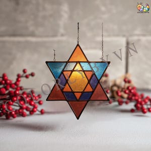 May include: A multi-coloured stained glass Star of David, suspended by a chain. The star features orange, blue, purple, and yellow glass panels. The background is a neutral grey, with red berries visible in the foreground.