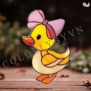May include: A stained glass duck with a pink bow. The duck is yellow, orange, and cream-colored with black eyes. The text "COLORLYBYVN" is visible on the left side of the image. The duck is standing on a wooden surface.