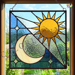 Op de afbeelding: Gebrandschilderd glaspaneel met een zon- en maanontwerp. De zon is geel met puntige stralen en de maan heeft een halvemaanvorm. Het paneel heeft blauwe, witte en groene accenten, met een donkerbruine rand en een ophangketting.