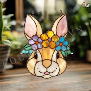 May include: Stained glass bunny with a floral crown. The bunny has a light brown face, pink ears, and a white muzzle. The floral crown features purple, yellow, and blue flowers with green leaves. The bunny is hanging from a metal loop.