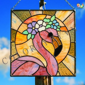 Könnte beinhalten: Quadratische Glasmalerei mit einem rosa Flamingo mit Blumenkrone. Der Hintergrund ist ein Sonnenstrahl-Design in Orange- und Gelbtönen. Der Flamingo hat einen schwarzen Schnabel, die Blumen sind weiß, lila und blau.