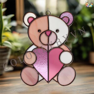 May include: Stained glass teddy bear ornament in shades of pink, white, and peach, holding a heart. The bear has a copper-colored outline and a small loop for hanging. A decorative item for a window or wall.