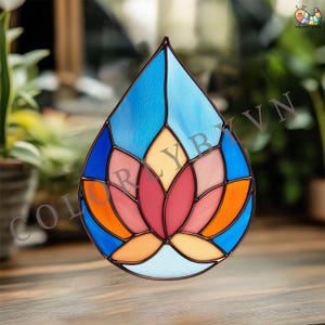 May include: Stained glass window art in a teardrop shape. The design features a lotus flower in shades of pink, red, orange, and yellow, set against a blue background. The piece is framed with a dark border and is suitable for home decor.