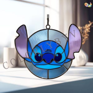 Könnte beinhalten: Buntglas-Fensterdekoration mit der Figur Stitch aus Lilo & Stitch. Das Design verwendet Blau- und Lilatöne mit einer schwarzen Umrandung. Die Fensterkunst wird an einer Kette aufgehängt. Das Wort "COLORLY" ist teilweise sichtbar.