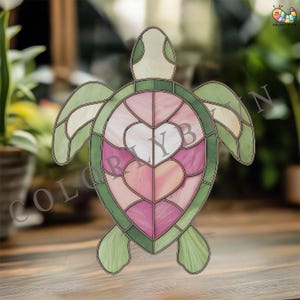 Peut inclure: Un vitrail en forme de tortue avec un motif de cœur. La tortue présente une carapace et des nageoires vertes, avec un motif de cœur rose et blanc au centre. Le texte "COLORFULBIN" est visible.
