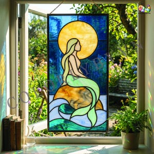 Pode incluir: Painel de vitral com uma silhueta de sereia com um sol amarelo ao fundo. A sereia tem cabelo loiro comprido e uma cauda verde, sentada numa rocha sobre ondas azuis e brancas. O painel é emoldurado em preto.