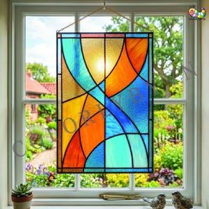 Peut inclure: Un vitrail rectangulaire avec un motif abstrait vibrant. Le panneau présente un mélange de couleurs, notamment orange, bleu, jaune et turquoise, disposées en formes courbes et géométriques. Il est suspendu devant une fenêtre avec vue sur un jardin.