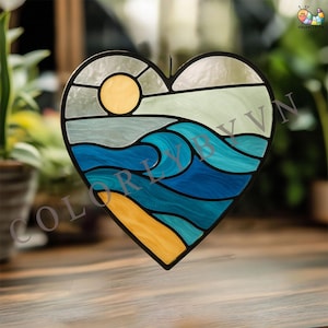May include: Heart-shaped stained glass window art depicting a beach scene with a yellow sun, blue waves, and a yellow sandy shore. The artwork has a black border and the text "COLORLYBYVN".