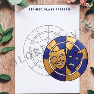 May include: A stained glass pattern featuring comedy and tragedy masks in gold and blue. The masks are set within a circular design, with a chain for hanging. The background shows a line drawing of the same design, with the text "STAINED GLASS PATTERN".