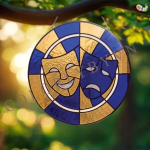 May include: A round stained glass piece featuring the comedy and tragedy theater masks. The masks are gold and blue, with a white border and a blue and gold checkered pattern around the edge. The piece hangs from a chain.