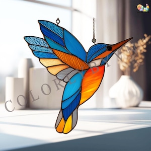 Peut inclure: Un colibri en vitrail aux ailes bleues, oranges et jaunes. L'oiseau est suspendu par une chaîne, idéal pour la décoration de fenêtre ou de mur. Le mot "COLOR" est visible sur le côté gauche de l'image.