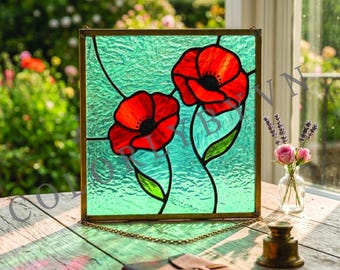 May include: Stained glass panel featuring two red poppy flowers with black centers and green stems against a textured turquoise background. The panel is framed in gold and hangs by a delicate chain. A notebook and small brass bell sit on a wooden surface.