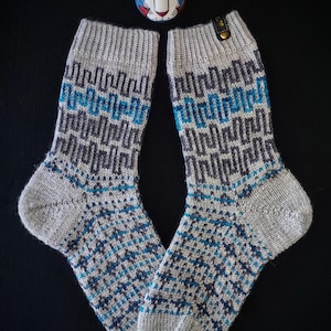 May include: A pair of gray knit socks with a geometric pattern in blue and dark gray. The socks have a ribbed cuff and a patterned design on the foot and leg. A small blue cat figurine is at the top of the image.