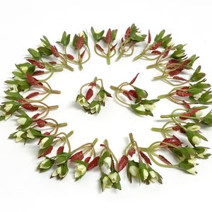 May include: A circle of artificial green floral stems with small white flowers and red leaves. The stems are arranged in a circle with the flowers facing outwards.