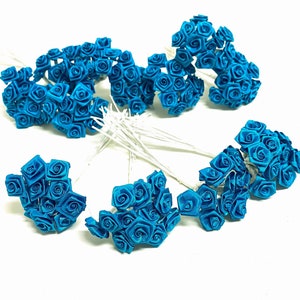 May include: A bunch of teal blue silk rose flower heads on wire stems. The roses are arranged in a starburst pattern.