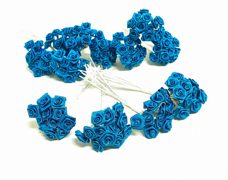 May include: A bunch of teal blue silk rose flower heads on wire stems. The roses are arranged in a starburst pattern.