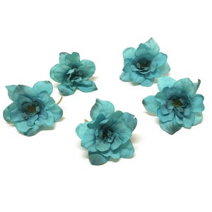 May include: Five teal blue artificial flowers with five petals each. The flowers are arranged in a circle on a white background.