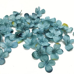 Pode incluir: Uma dispersão de pétalas de flores de seda azul-esverdeado, perfeitas para artesanato ou decoração.