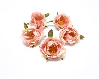 May include: Five blush pink artificial rose flower buds with green leaves. The flowers are arranged in a circle on a white background.