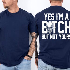 Op de afbeelding: Marineblauw T-shirt met de tekst "YES I'M A BITCH BUT NOT YOURS" en een schedelafbeelding op de achterkant. De voorkant van het T-shirt is effen marineblauw. Het T-shirt heeft een ronde hals.