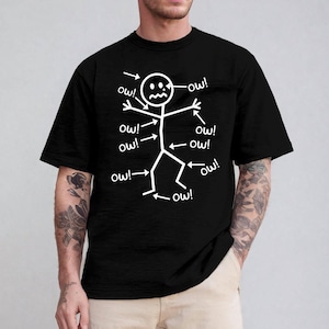 Pode incluir: Camiseta preta com um desenho de boneco de palito branco. Setas apontam para as partes do corpo do boneco de palito, cada uma com "ow!". O boneco de palito tem uma expressão angustiada. Uma camiseta gráfica humorística.