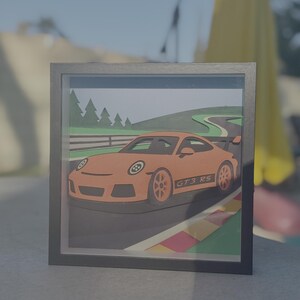 Pode incluir: Obra de arte de um carro GT3 RS laranja em uma moldura preta. A imagem mostra o carro em uma pista de corrida com detalhes verdes e vermelhos. O carro tem detalhes pretos e o texto "GT3 RS" na lateral.