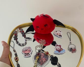 May include: A selection of accessories, including a red plush devil, keyrings, and stickers, arranged on a heart-shaped mirror tray with a gold rim. The keyrings feature beads, charms, and the word "stylus".