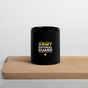 Op de afbeelding: Zwarte keramische koffiemok met de tekst "ARMY NATIONAL GUARD" in gele letters en een gele ster.
