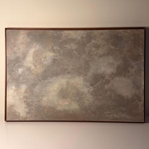 Puede incluir: Pintura abstracta rectangular con marco de madera marrón. La obra presenta un diseño nublado y texturizado en tonos grises, beige y blanco, creando un efecto suave y atmosférico. La pintura se exhibe sobre un fondo neutro.