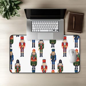 May include: A rectangular desk mat featuring a repeating pattern of watercolor-style nutcracker figures in various uniforms of red, blue, and green. The nutcrackers are depicted with tall hats, detailed jackets, and boots, arranged on a white background.