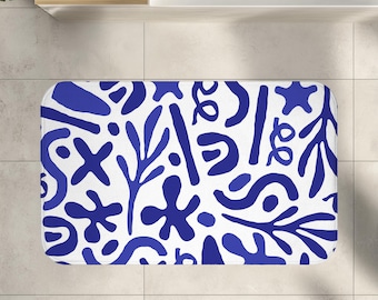 May include: Rectangular white bath mat with a repeating pattern of blue abstract shapes, including floral and geometric designs. The mat is designed for bathroom use and features a non-slip backing.