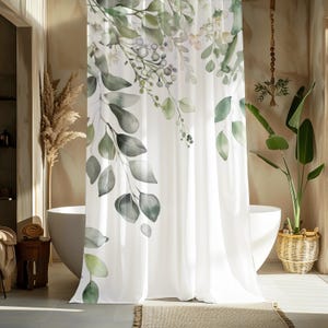 Puede incluir: Cortina de ducha blanca con un diseño de acuarela de hojas y bayas de eucalipto verdes y grises. La cortina cuelga frente a una bañera blanca, con una cesta de mimbre y una planta en maceta en el fondo.