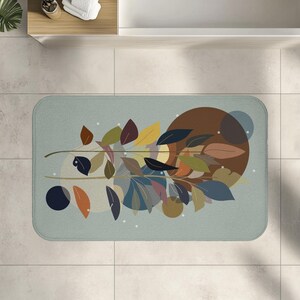 Puede incluir: Una alfombra de baño rectangular con fondo azul claro. La alfombra presenta un diseño botánico estilizado con hojas coloridas en tonos marrón, amarillo, azul y naranja. Un círculo marrón grande y círculos azules más pequeños también forman parte del diseño.