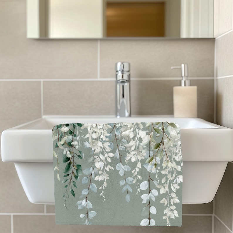 a bathroom sink with a white towel hanging on it, which has a green and white floral design. The sink is positioned in front of a mirror, and there is a soap dispenser on the right side of the sink.