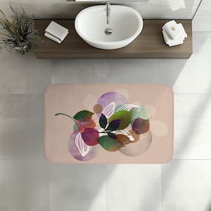 May include: A rectangular bath mat with a floral design. The mat features a light pink background with a cluster of leaves in shades of green, purple, and red. The leaves are arranged over overlapping circles in muted tones.