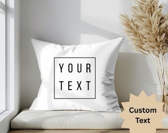 Könnte beinhalten: Weißes quadratisches Kissen mit dem Text "YOUR TEXT" in einem schwarzen Quadrat. Ein beigefarbener sternförmiger Anhänger mit den Worten "Custom Text" befindet sich auf der rechten Seite. Das Kissen liegt auf einer Holzbank.