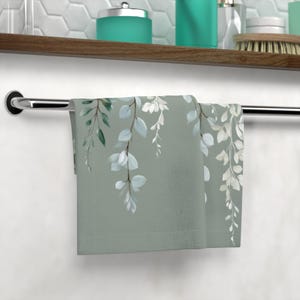 A towel with a green and white leaf pattern is hanging on a metal towel rack in a bathroom.