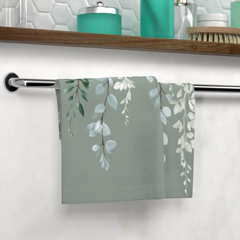 A towel with a green and white leaf pattern is hanging on a metal towel rack in a bathroom.