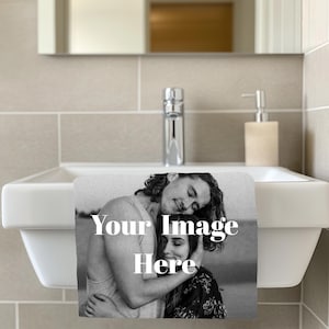 Pode incluir: Uma toalha de mão branca com o texto "Your Image Here" em um banheiro. A toalha apresenta uma imagem em preto e branco de um casal se abraçando. Uma torneira cromada e um dispensador de sabão são visíveis.