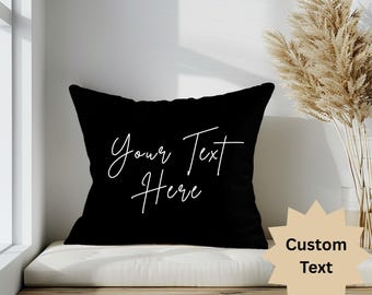 Könnte beinhalten: Schwarzes quadratisches Kissen mit dem Text "Your Text Here" in weißer Schrift. Ein sternförmiges Schild in Beige mit den Worten "Custom Text" befindet sich auf der rechten Seite. Das Kissen liegt auf einer Holzbank.