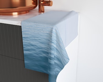 May include: A blue and white patterned decorative towel is draped over a white surface. The towel has a water-like design. A copper-colored sink and faucet are visible in the background.