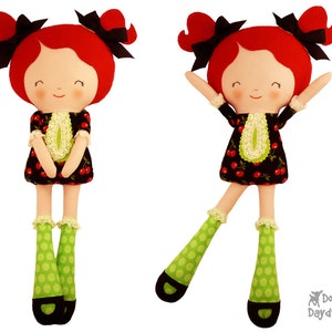 Puede incluir: Dos muñecas de fieltro con pelo rojo, lazos negros y piernas con lunares verdes. Las muñecas llevan vestidos negros con ribetes de encaje blanco y estampado de cerezas. La muñeca de la izquierda está de pie recta, mientras que la muñeca de la derecha está de pie con una pierna levantada.